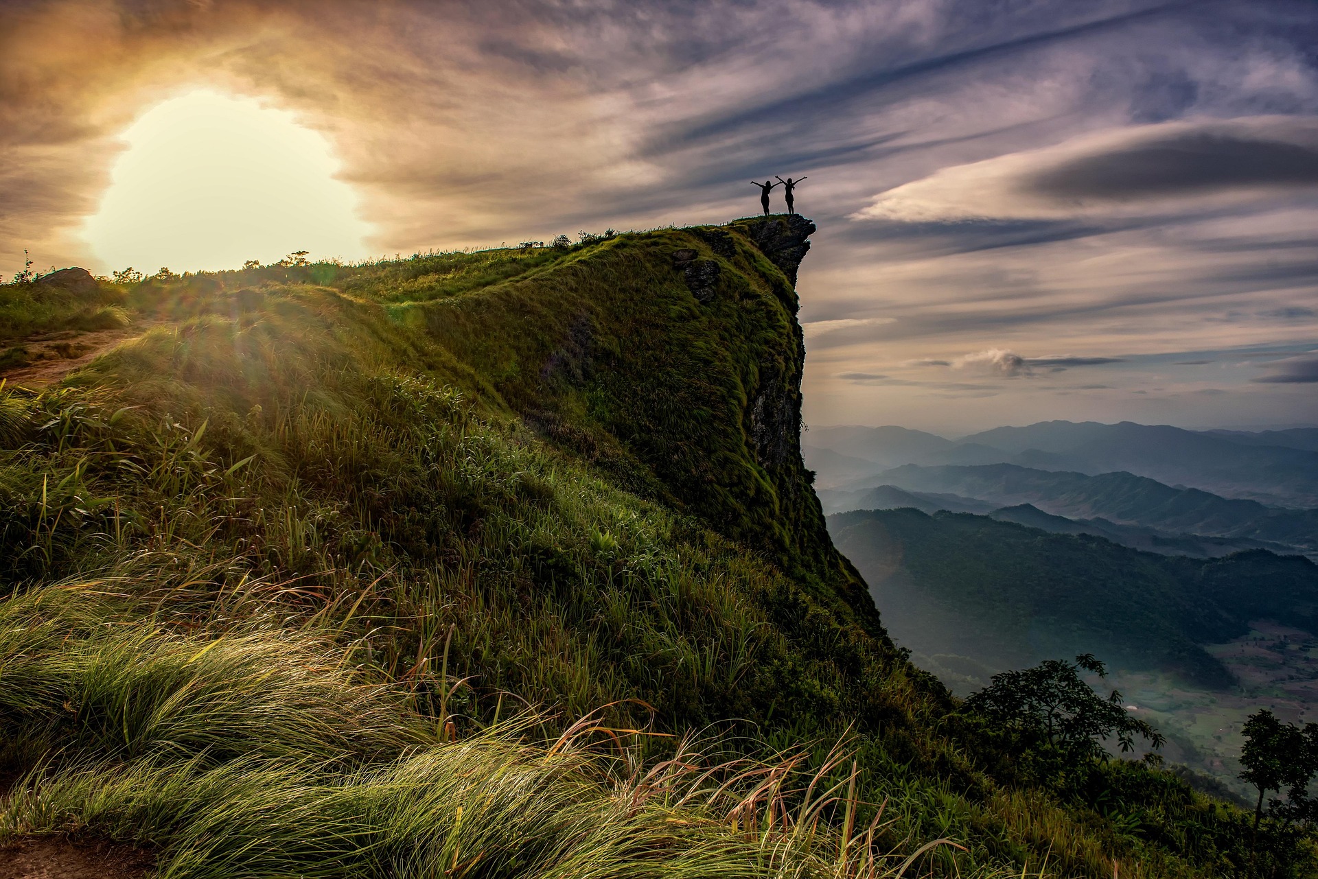 Two people celebrating on a mountain cliff at sunset